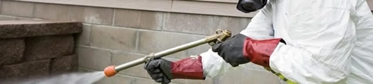 Pest control technician applying exterior insect treatment along a home foundation in Tempe, AZ