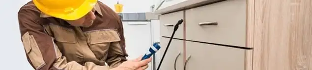 Roach exterminator applying treatment under kitchen cabinets in Tempe, AZ