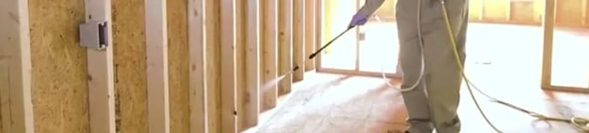 Termite treatment technician applying spray along framing and unfinished walls in Tempe, AZ