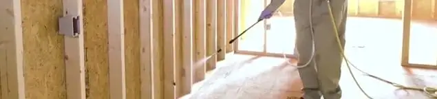 Termite treatment technician applying spray along framing and unfinished walls in Tempe, AZ